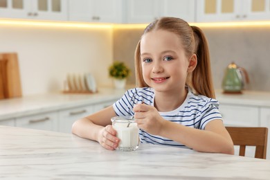 Cute little girl with tasty yogurt at white marble table in kitchen