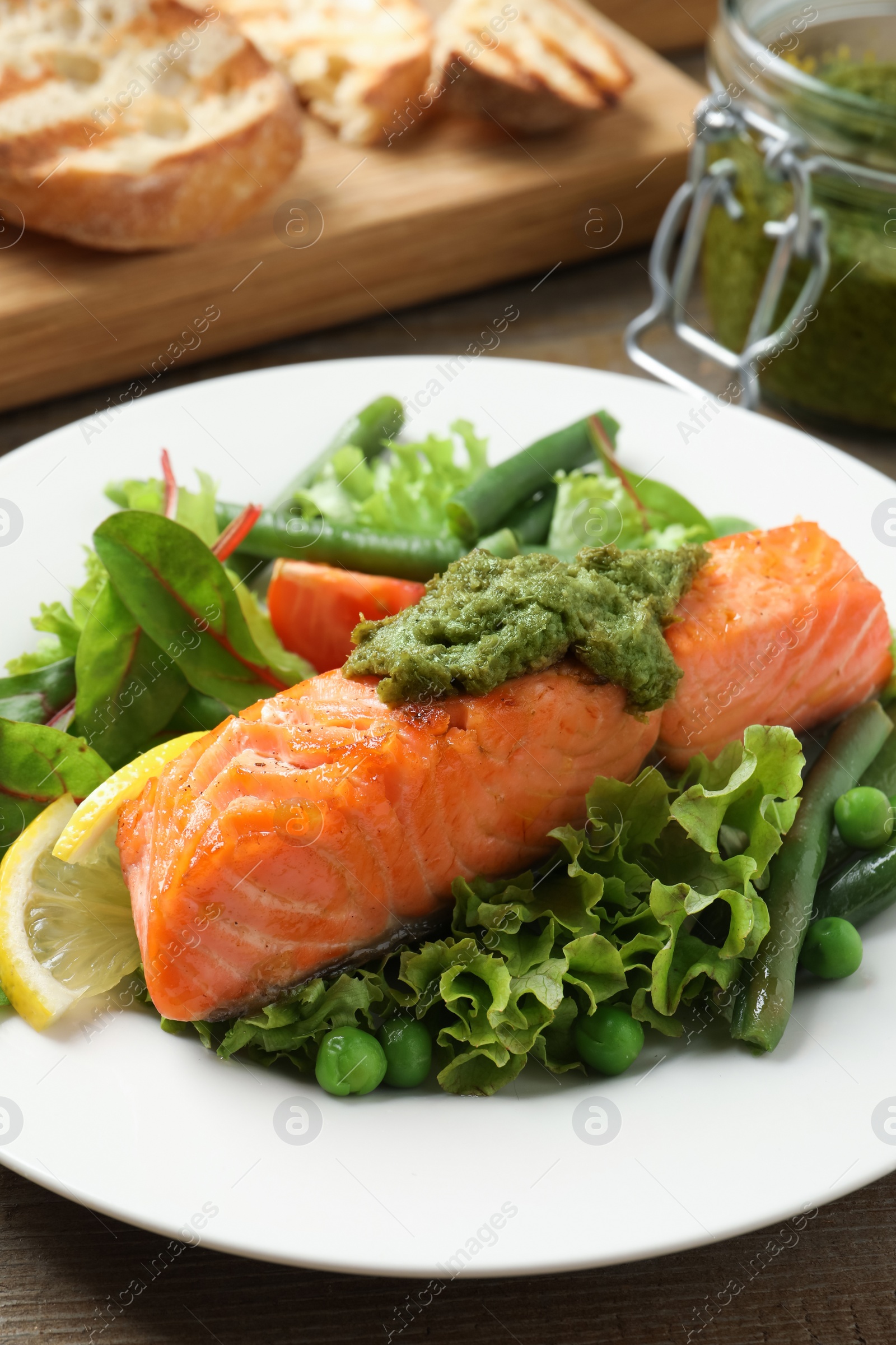 Photo of Tasty cooked salmon with pesto sauce served on wooden table, closeup