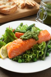 Photo of Tasty cooked salmon with pesto sauce served on wooden table, closeup