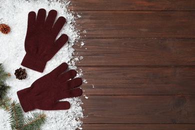 Stylish woolen gloves and winter decor on wooden table, flat lay. Space for text