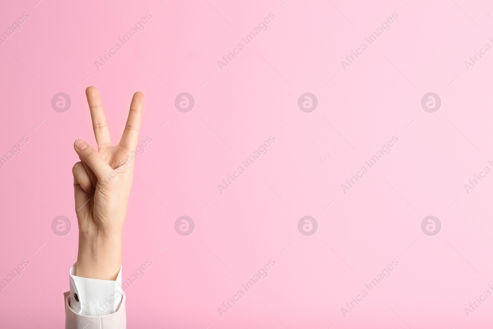 Photo of Young woman showing victory gesture on color background. Space for text