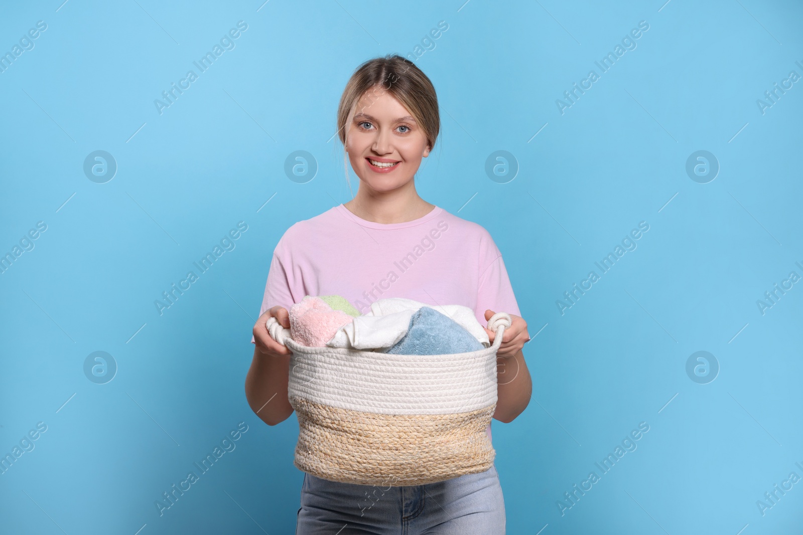 Photo of Happy woman with basket full of laundry on light blue background