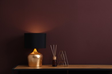 Photo of Wooden table with decor and lamp near brown wall in room, space for text