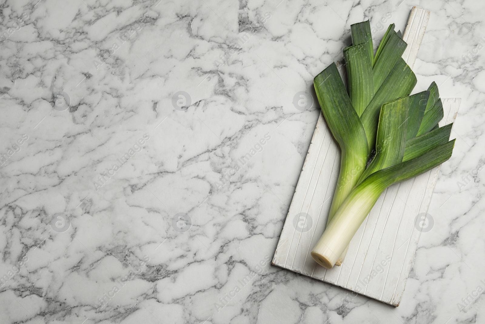 Photo of Fresh raw leeks on marble table, flat lay with space for text. Ripe onion