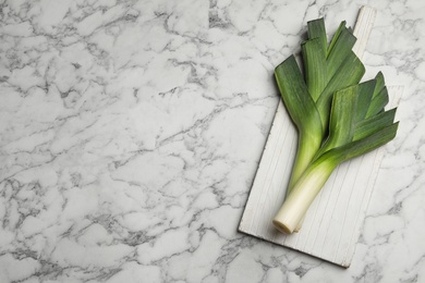 Fresh raw leeks on marble table, flat lay with space for text. Ripe onion