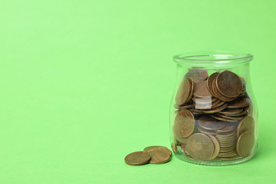 Photo of Glass jar with coins on light green background, space for text
