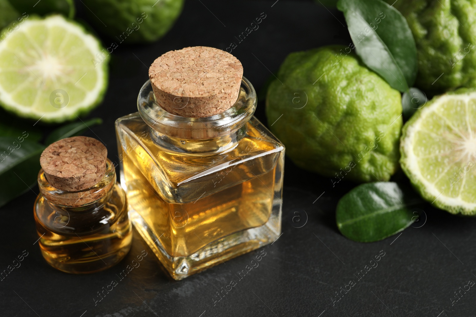 Photo of Glass bottles of bergamot essential oil and fresh fruits on black stone table