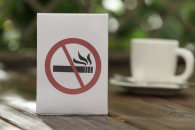Photo of No Smoking sign and cup of drink on wooden table against blurred background, closeup