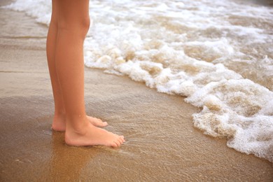 Photo of Little girl standing on sandy beach near sea, closeup. Space for text