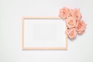 Photo of Empty photo frame and beautiful rose flowers on white background, flat lay. Mockup for design