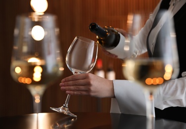 Waitress pouring wine into glass in restaurant, closeup