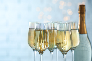 Glasses and bottle of champagne against blurred lights, closeup