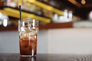 Photo of Glass with cola and ice cubes on table indoors. Space for text