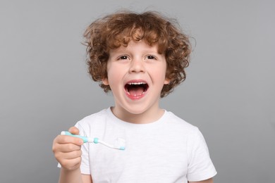 Photo of Cute little boy holding plastic toothbrush with paste on light grey background