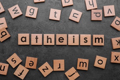 Word Atheism made of wooden squares with letters on grey textured table, flat lay