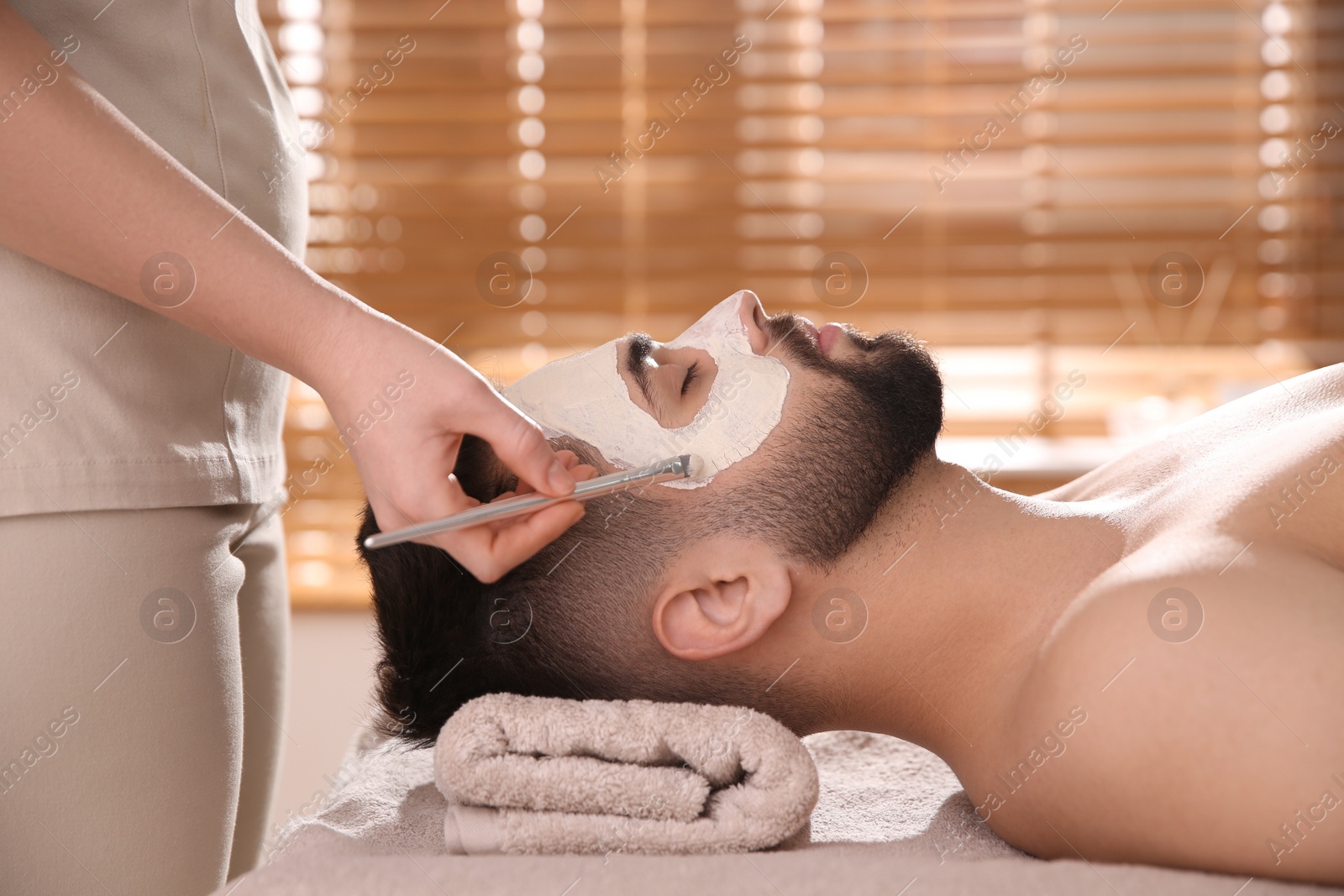 Photo of Cosmetologist applying mask on man's face in spa salon