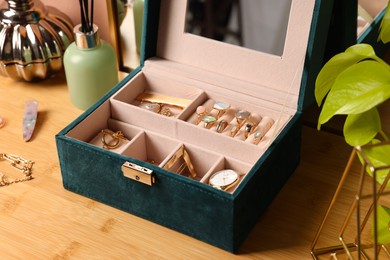 Photo of Elegant jewelry box with beautiful bijouterie and expensive wristwatch on wooden table