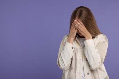 Photo of Resentful woman covering face with hands on violet background, space for text