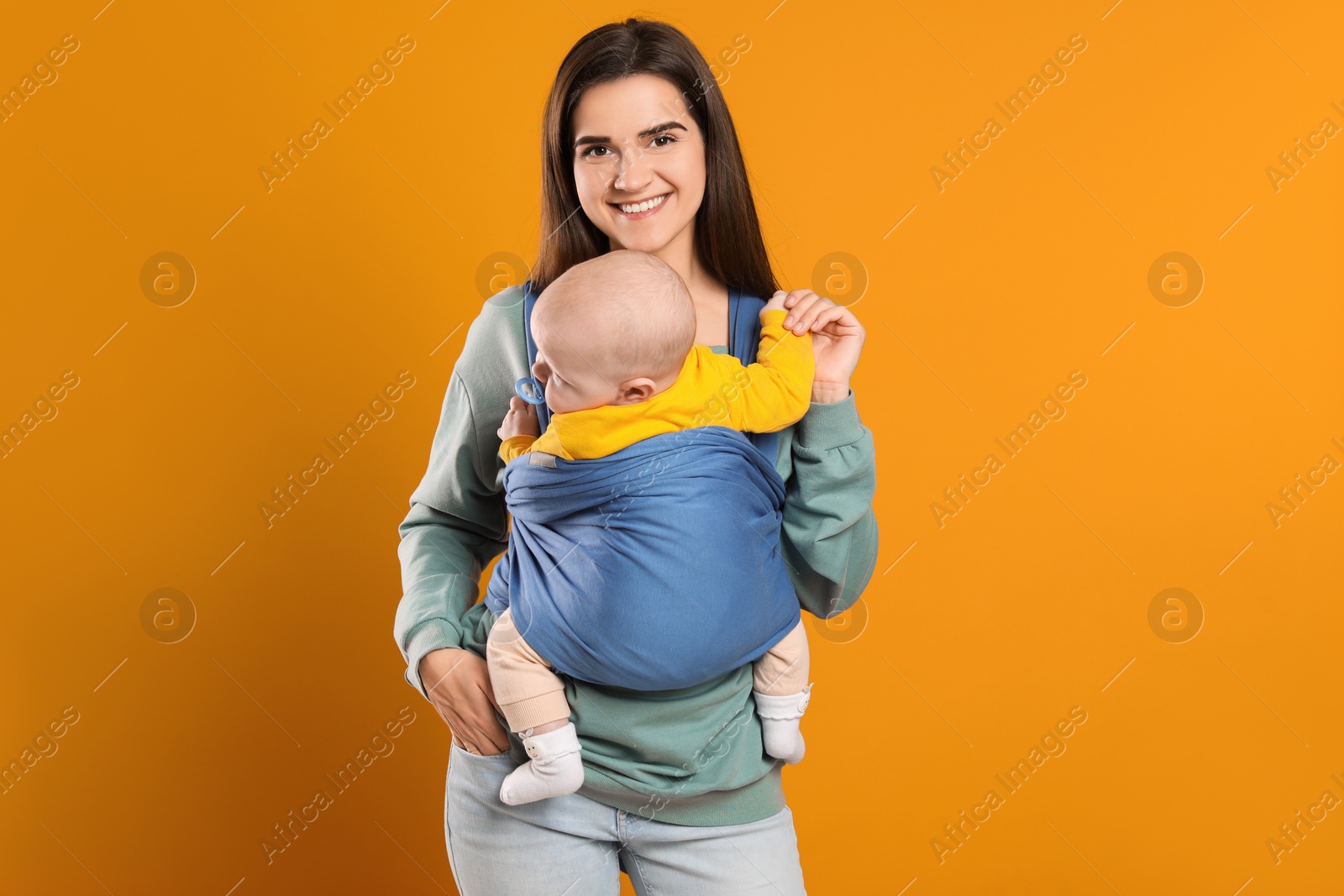 Photo of Mother holding her child in sling (baby carrier) on orange background