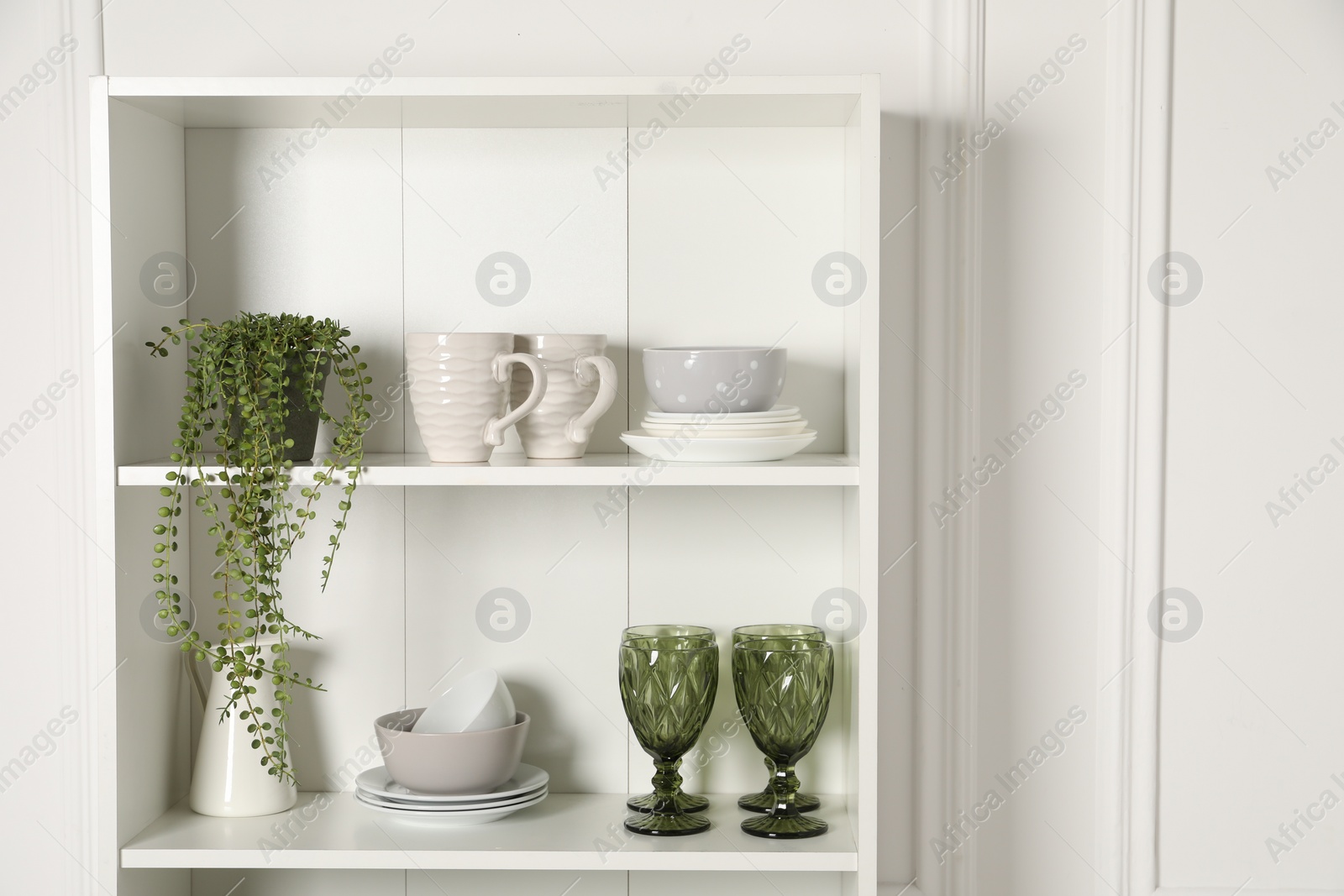 Photo of Different clean dishware and houseplant on shelves in cabinet indoors