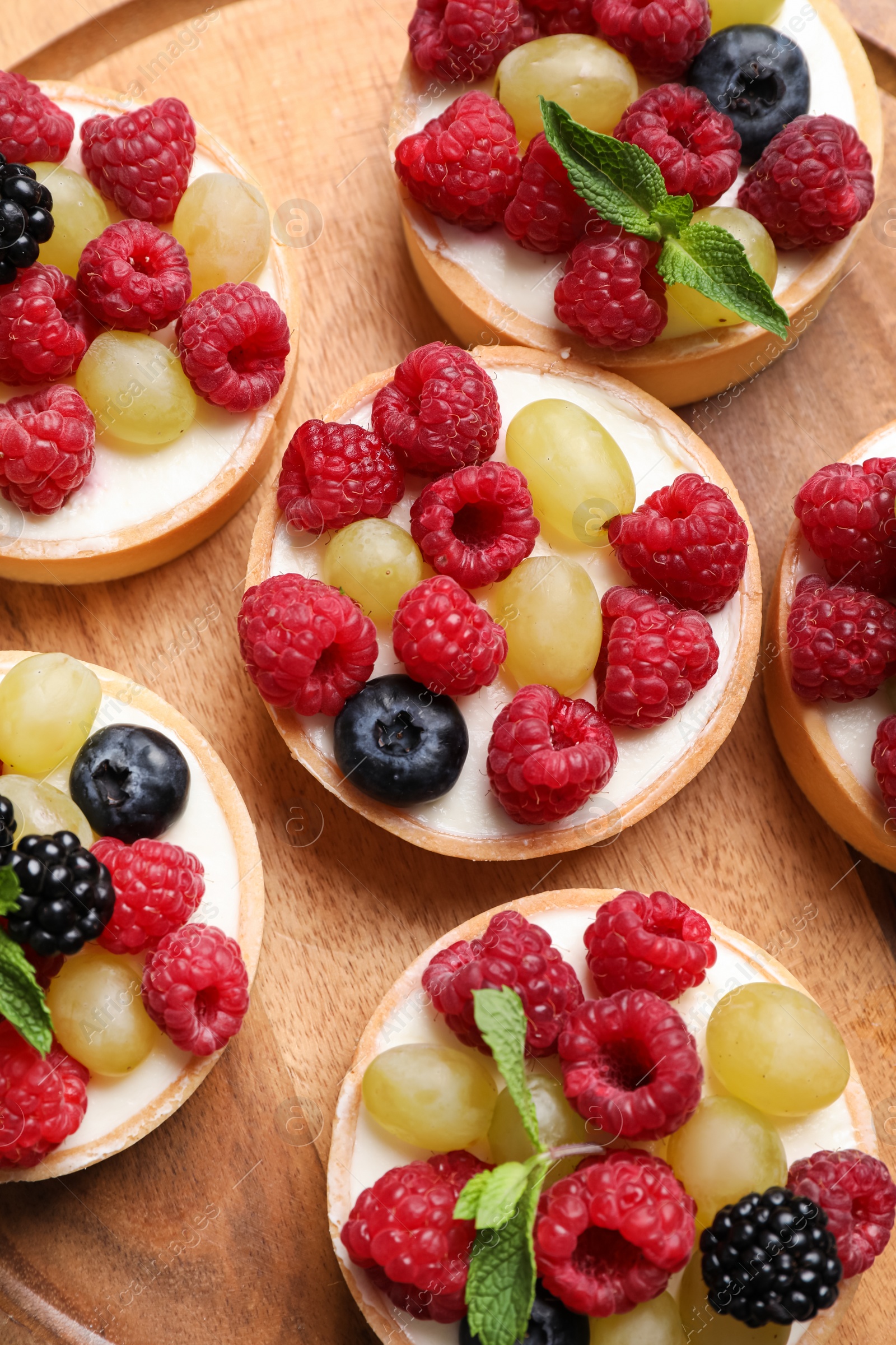 Photo of Delicious tartlets with berries on wooden board, flat lay