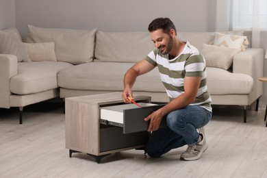 Man with screwdriver assembling nightstand on floor at home