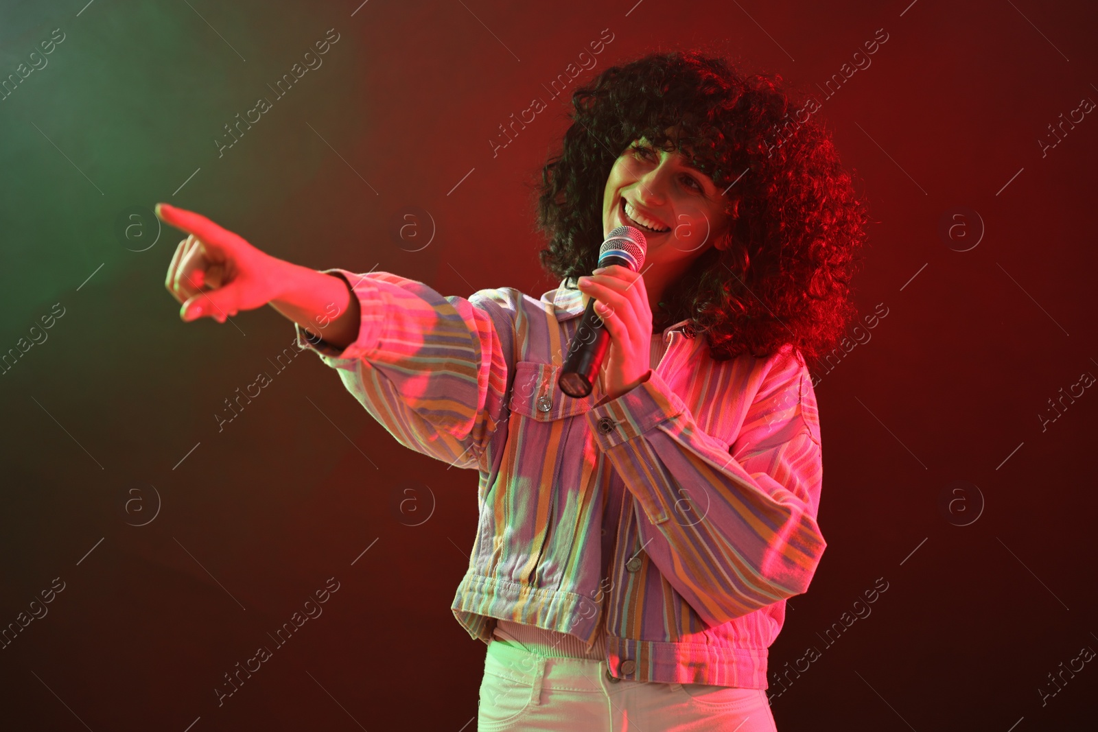 Photo of Beautiful young woman with microphone singing on color background in neon lights