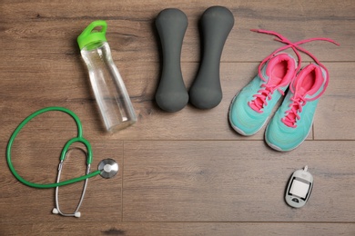 Flat lay composition with stethoscope, sport items and digital glucometer on wooden background. Diabetes prevention