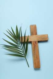 Photo of Wooden cross and palm leaf on light blue background, top view. Easter attributes