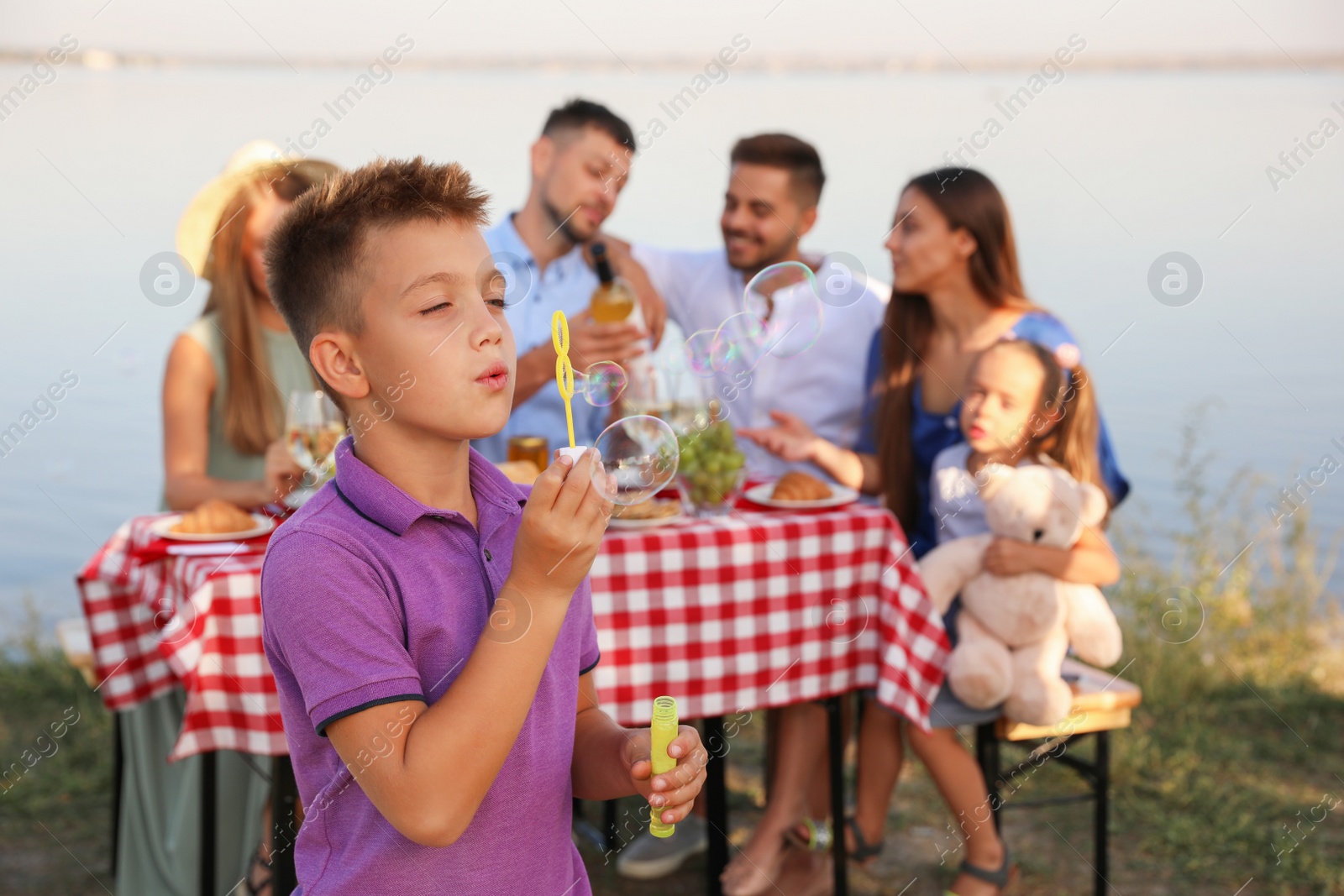 Photo of Little boy blowing bubbles outdoors. Picnic time