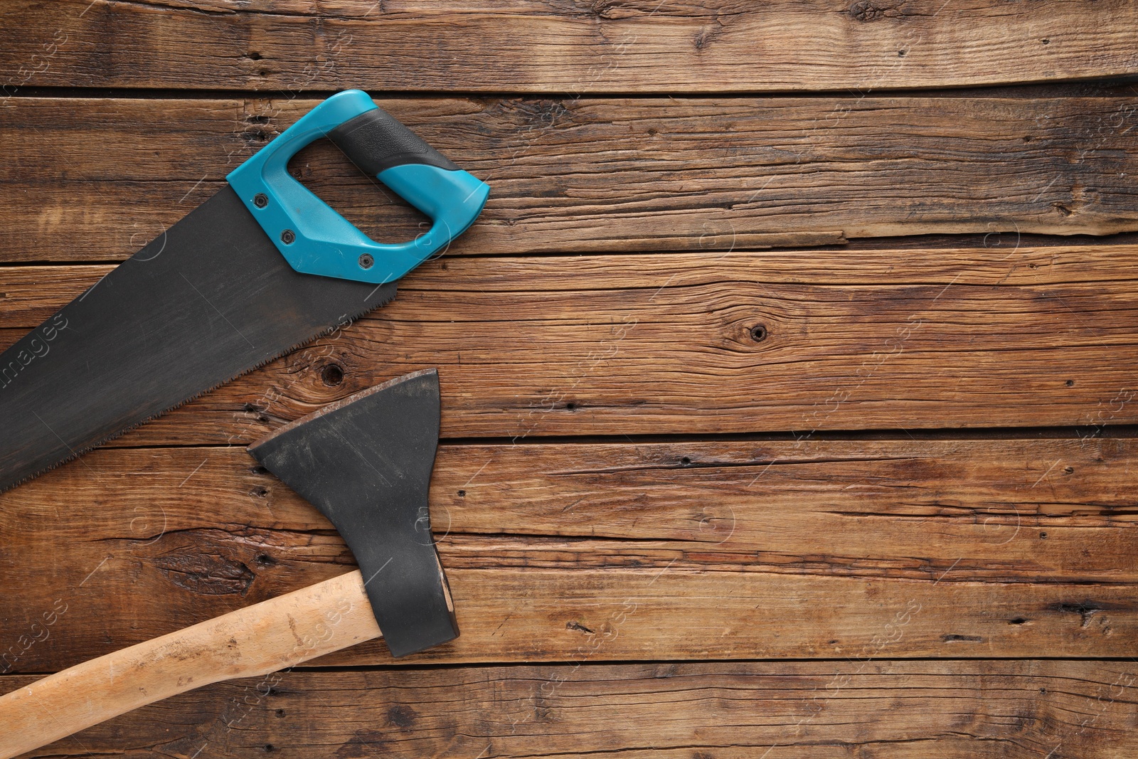 Photo of Saw with light blue handle and axe on wooden background, flat lay. Space for text