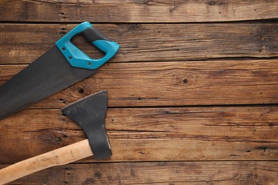 Saw with light blue handle and axe on wooden background, flat lay. Space for text