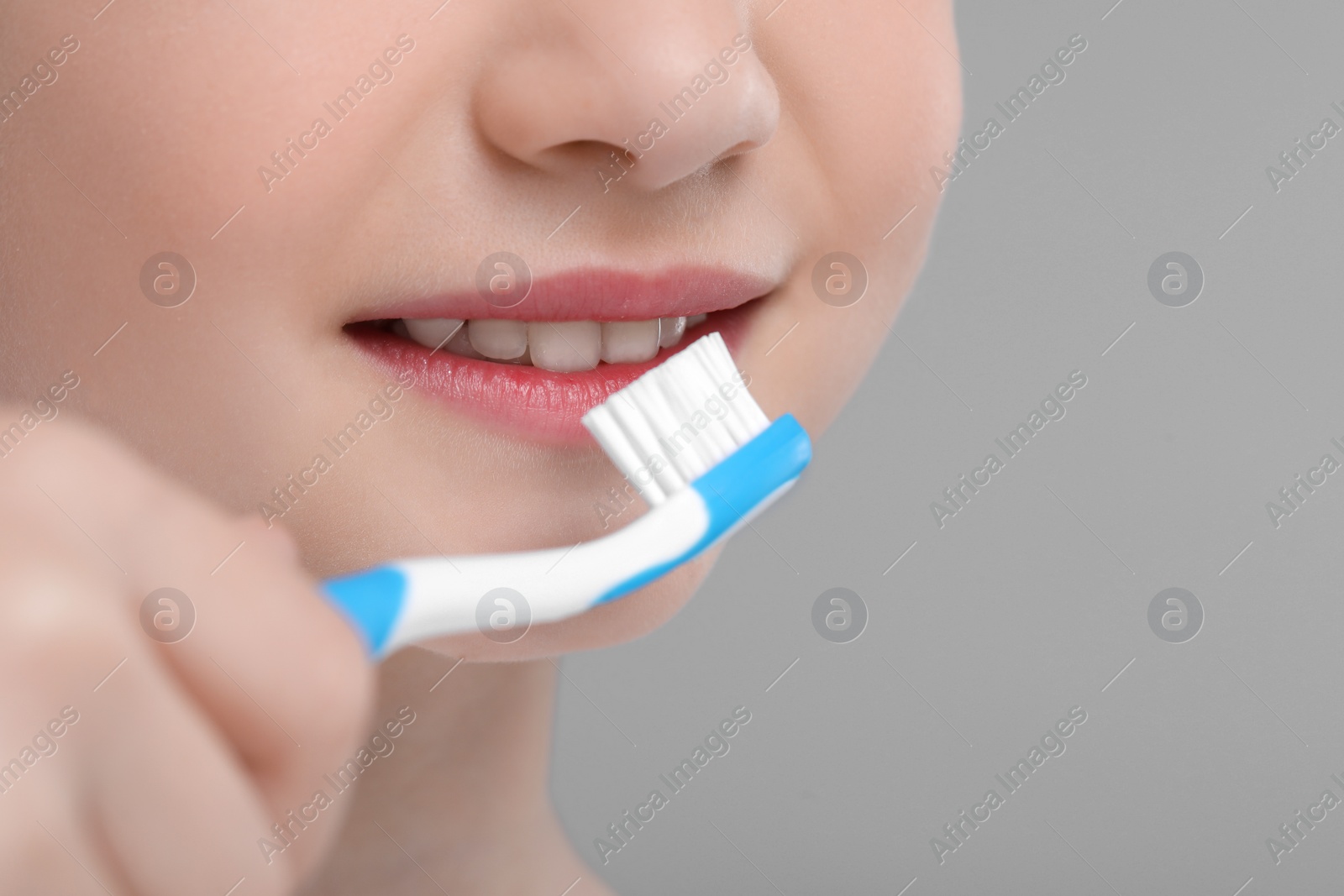 Photo of Girl brushing her teeth with toothbrush on light grey background, closeup. Space for text