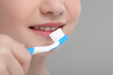 Girl brushing her teeth with toothbrush on light grey background, closeup. Space for text