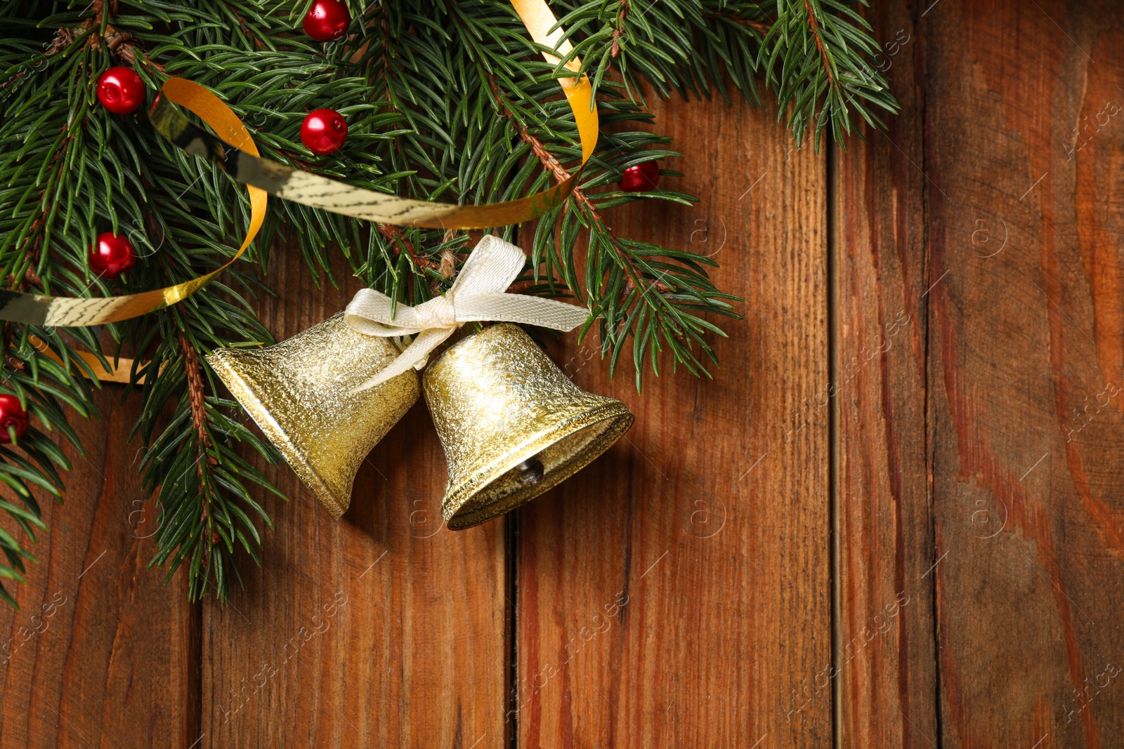 Photo of Christmas bells and fir tree branches on wooden table, flat lay. Space for text