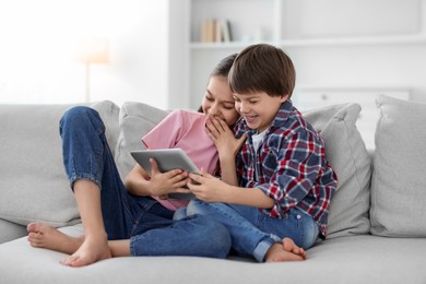 Happy brother and sister with tablet on sofa at home