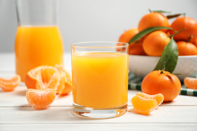 Glass of fresh tangerine juice and fruits on white wooden table