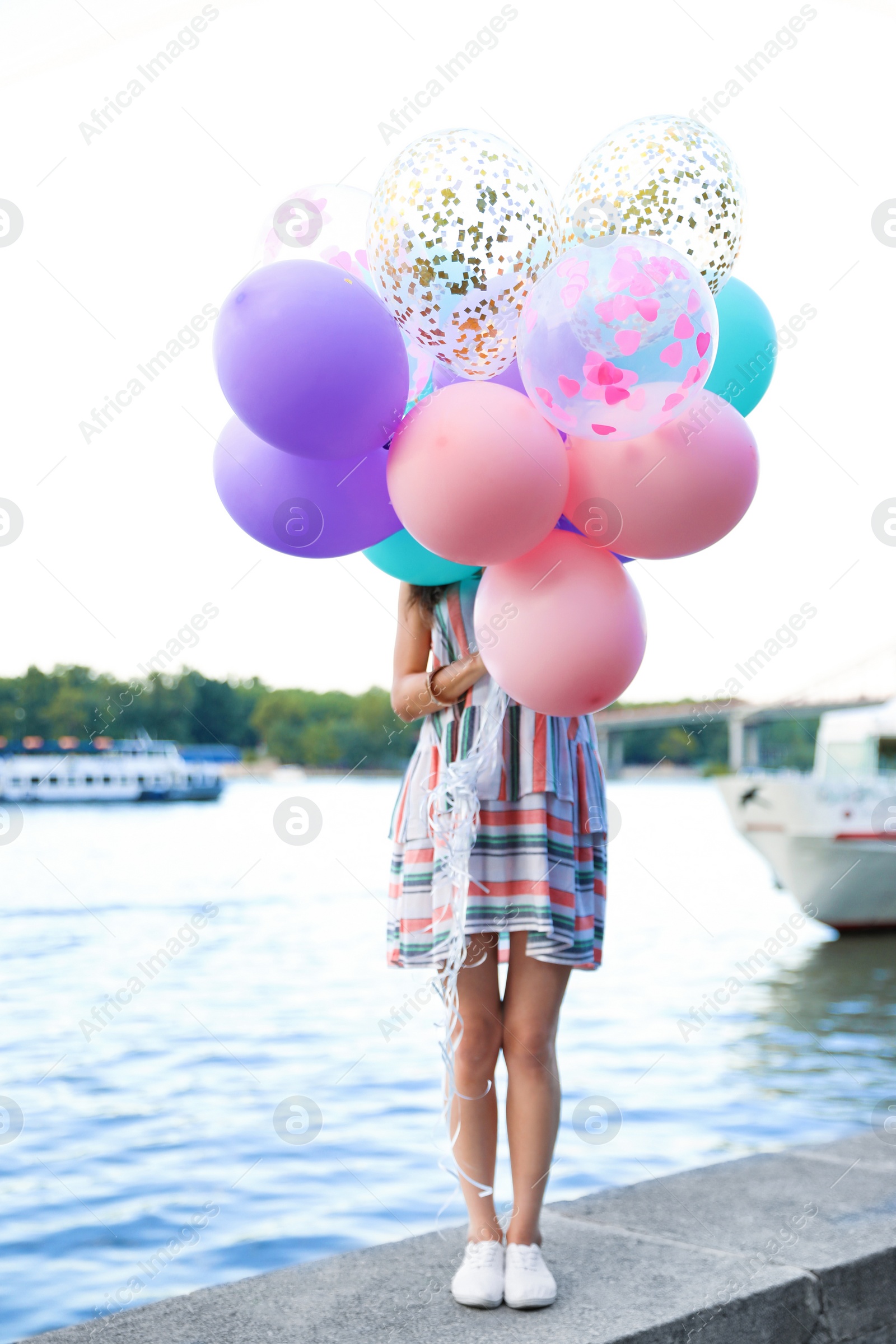 Photo of Young woman hiding behind color balloons near river