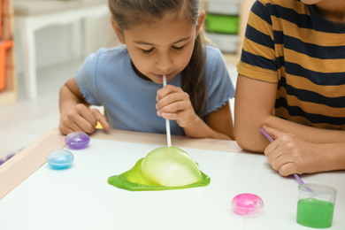 Photo of Children playing with slime at white table indoors, closeup