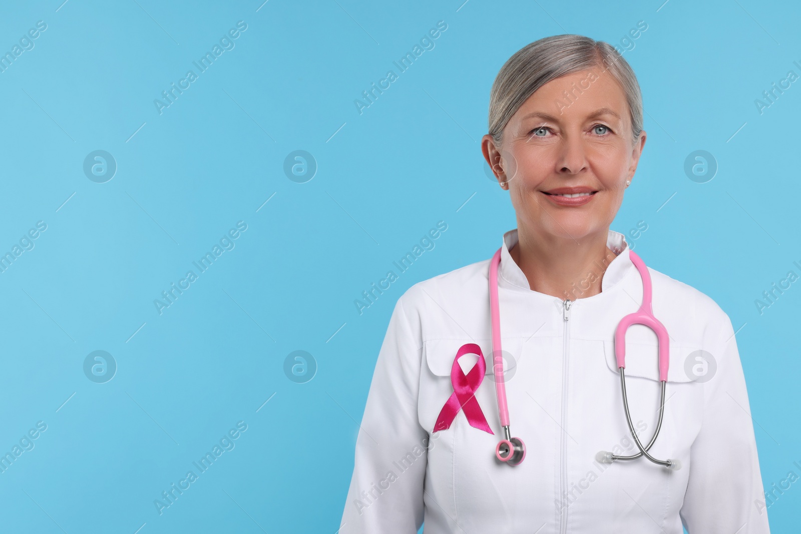 Photo of Doctor with pink ribbon and stethoscope on light blue background, space for text. Breast cancer awareness