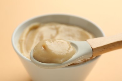 Photo of Eating healthy baby food with spoon on beige background, closeup