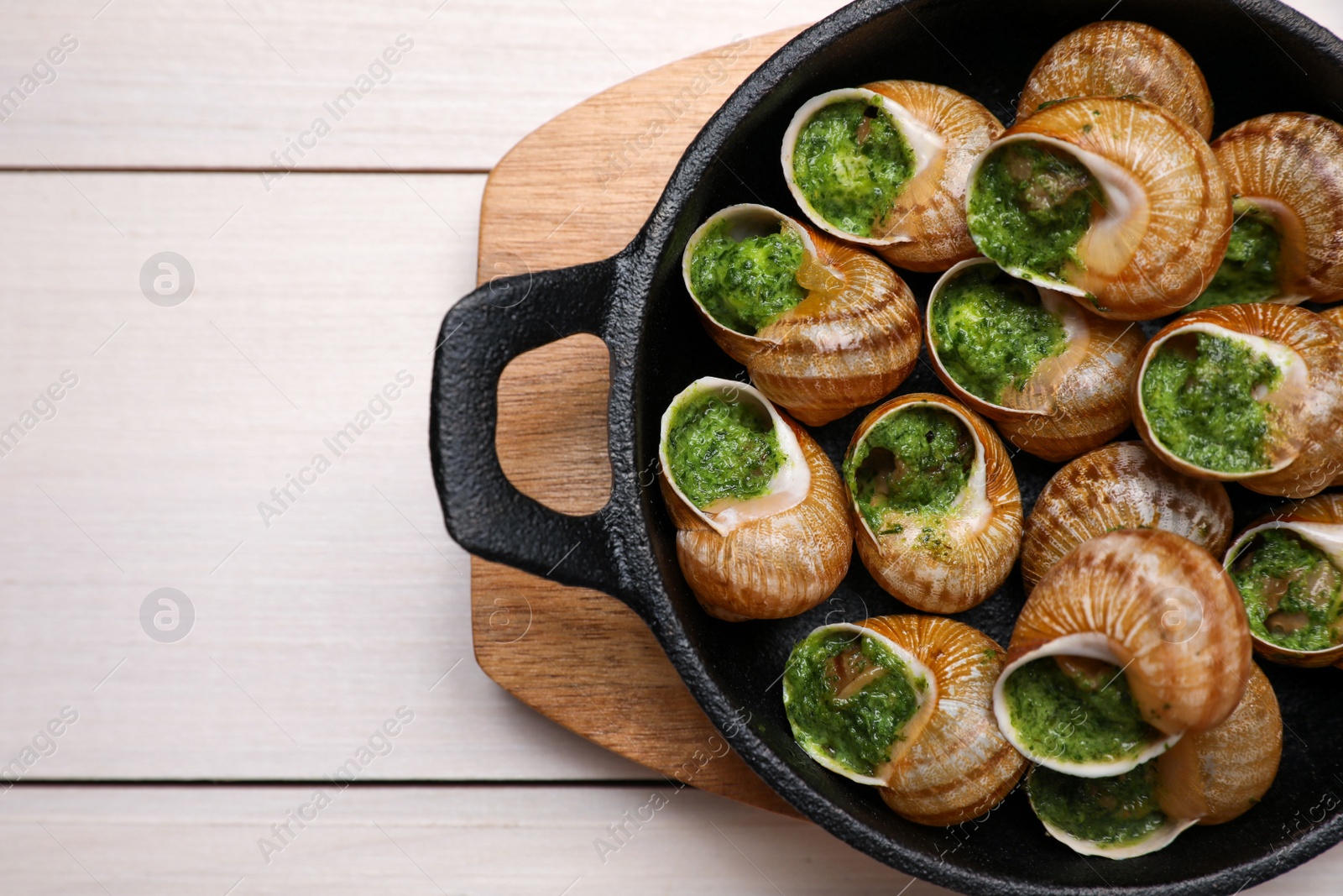 Photo of Delicious cooked snails served on white wooden table, top view. Space for text