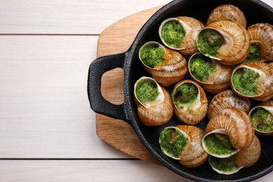 Photo of Delicious cooked snails served on white wooden table, top view. Space for text