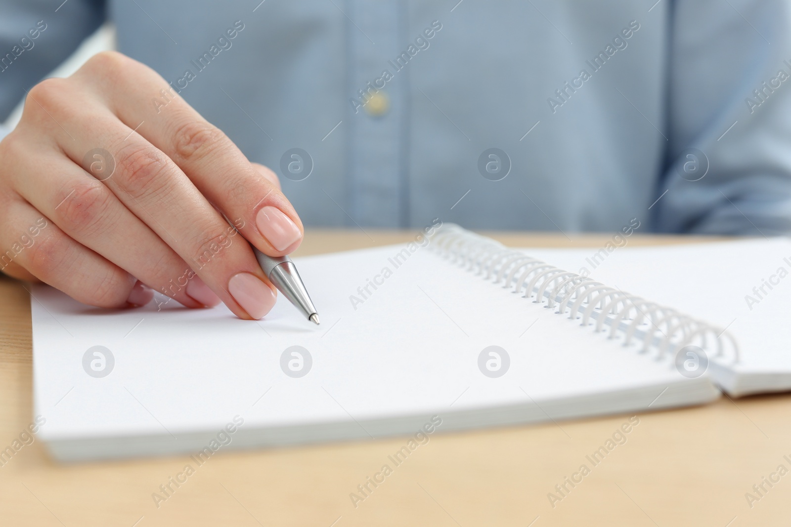 Photo of Woman writing in notebook at wooden table, closeup