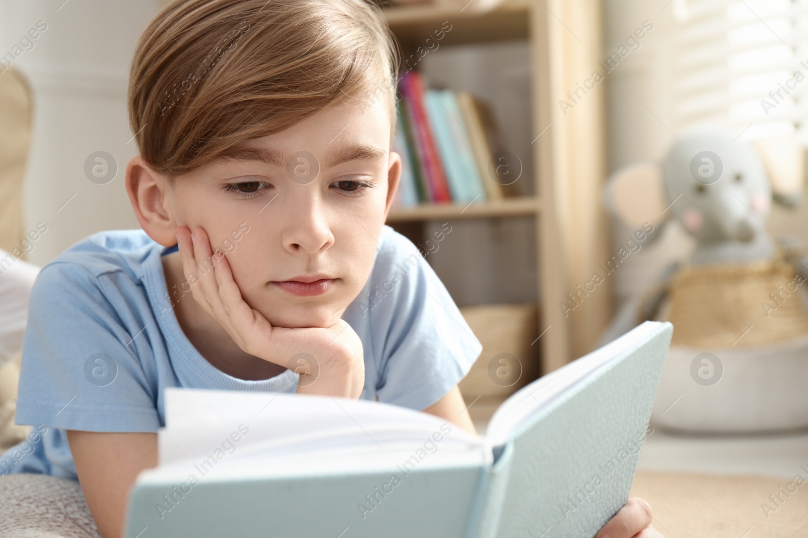 Photo of Little boy reading book on floor at home