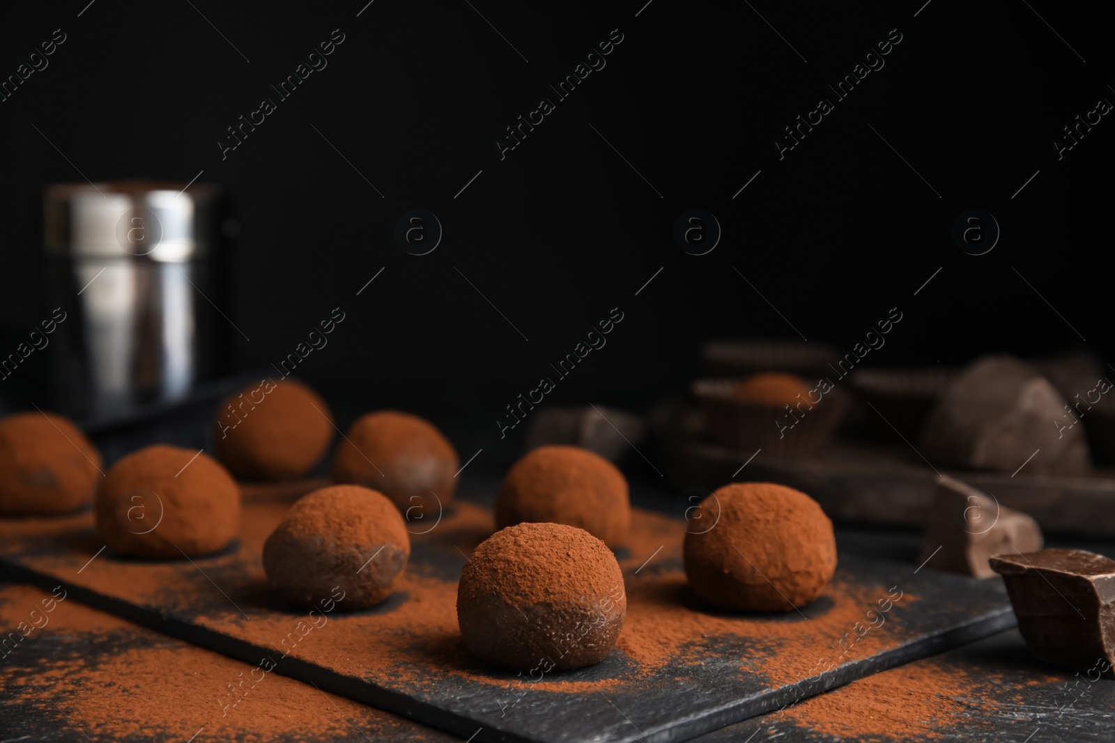 Photo of Delicious chocolate truffles powdered with cocoa on black table, space for text