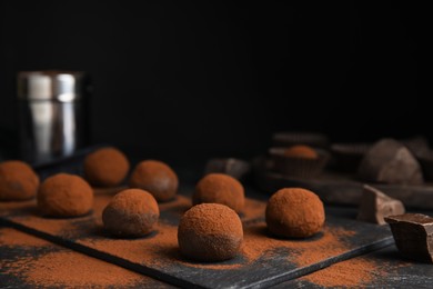 Photo of Delicious chocolate truffles powdered with cocoa on black table, space for text