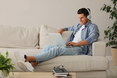 Man with laptop and headphones sitting on sofa at home