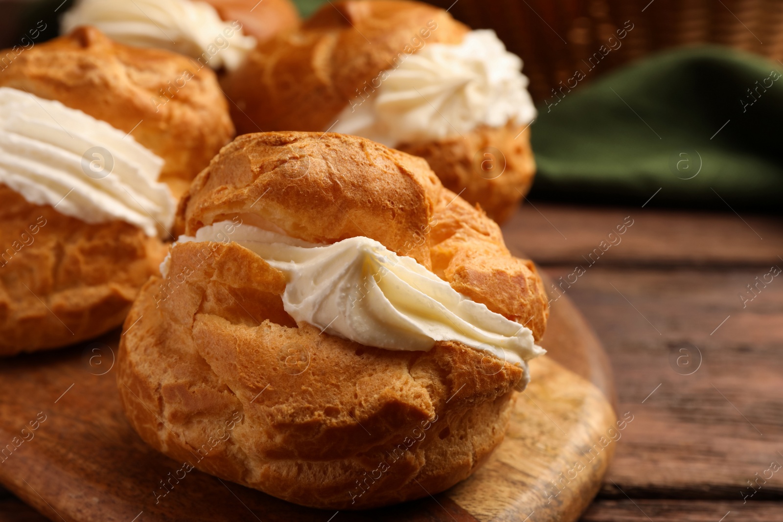 Photo of Delicious profiteroles with cream filling on wooden table, closeup