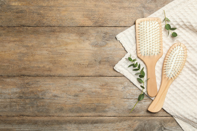 Photo of New hair brushes, twigs and towel on wooden background, flat lay. Space for text